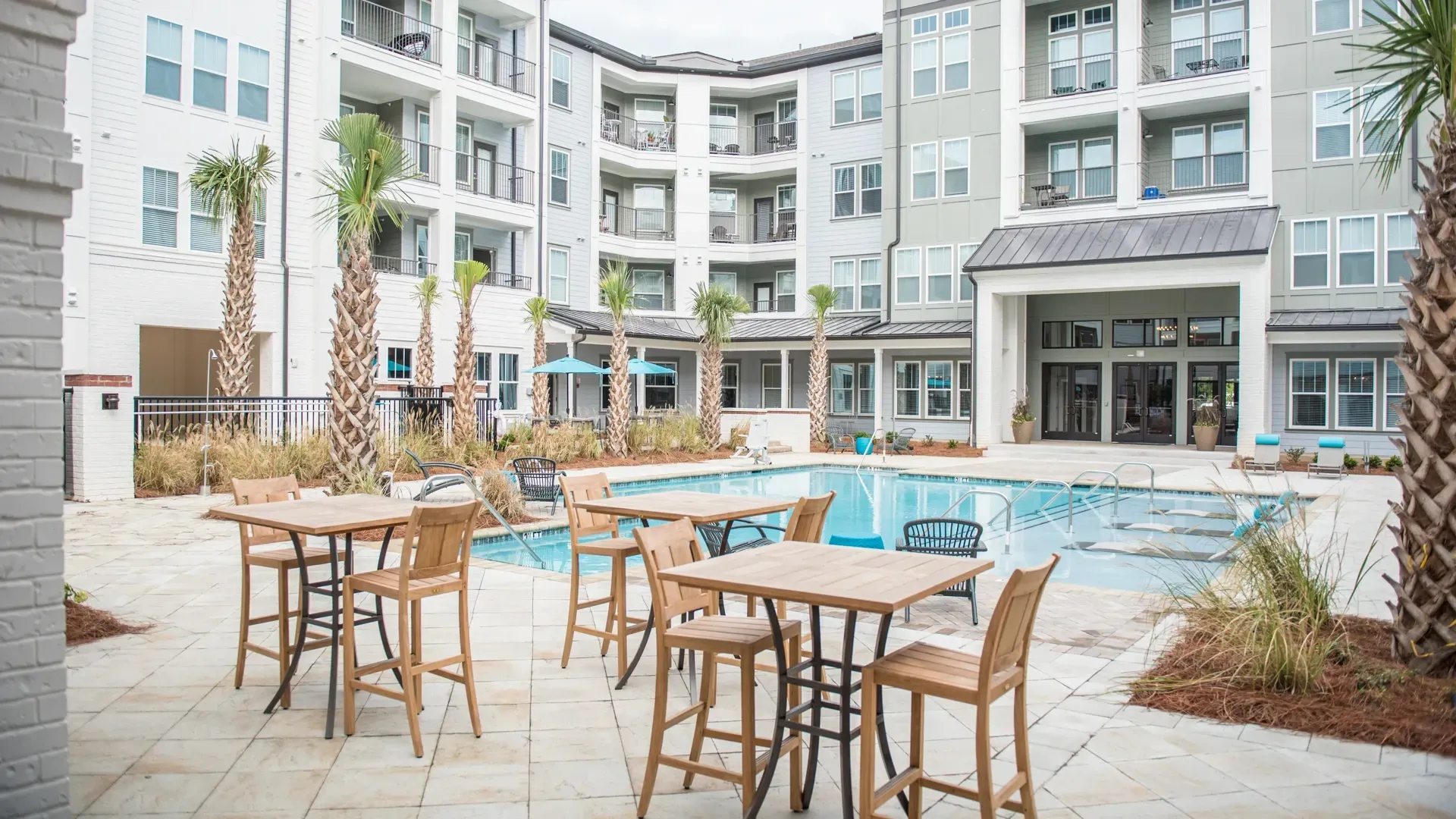Outdoor swimming pool and lounge area with tables and chairs at a multifamily property.