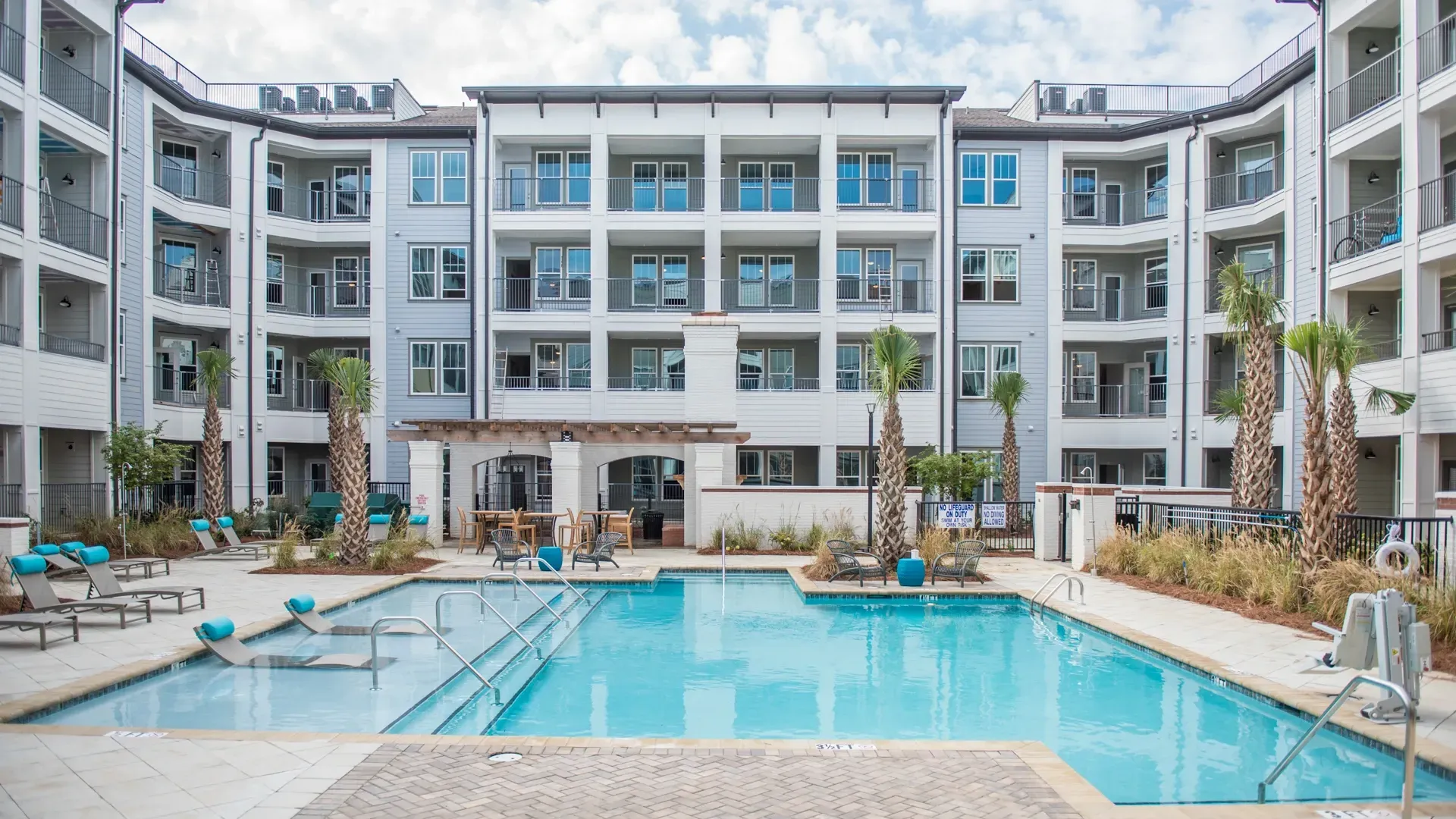 Exterior of apartment building with a swimming pool and lounge chairs.