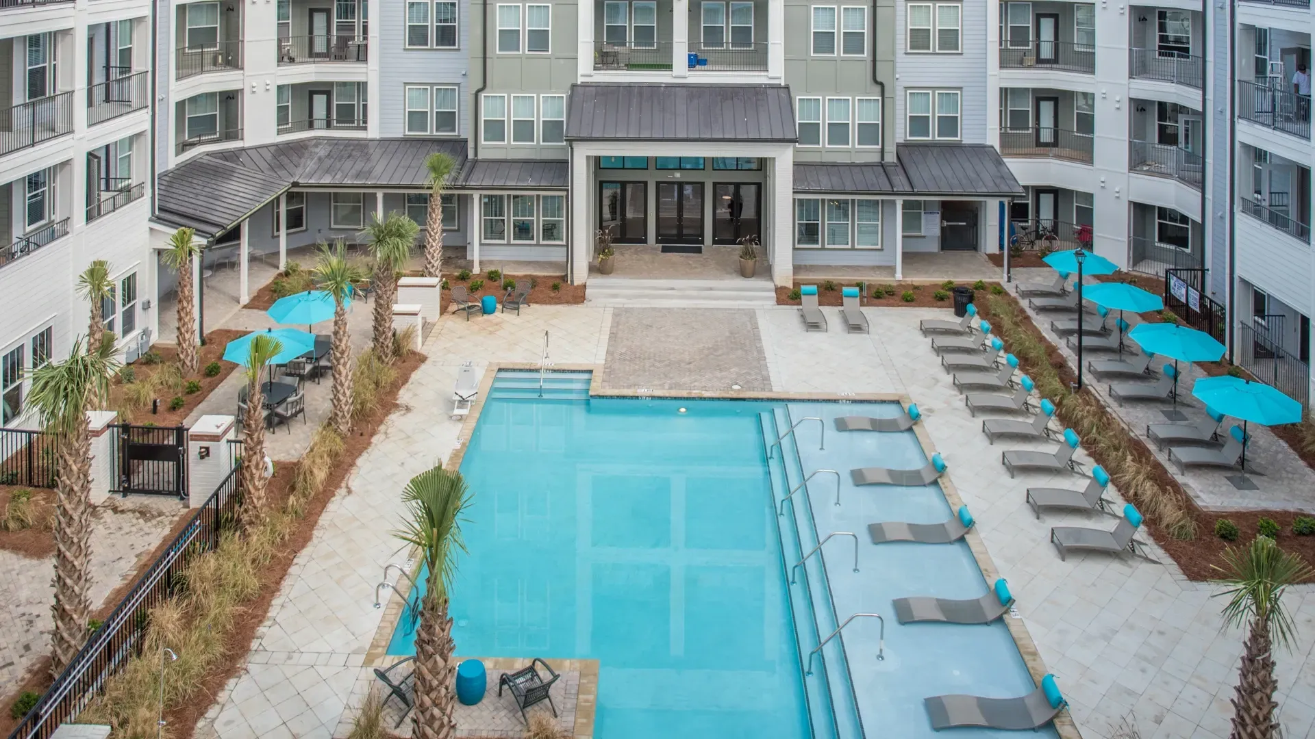 Resort-style swimming pool with lounge chairs and umbrellas at apartment complex.