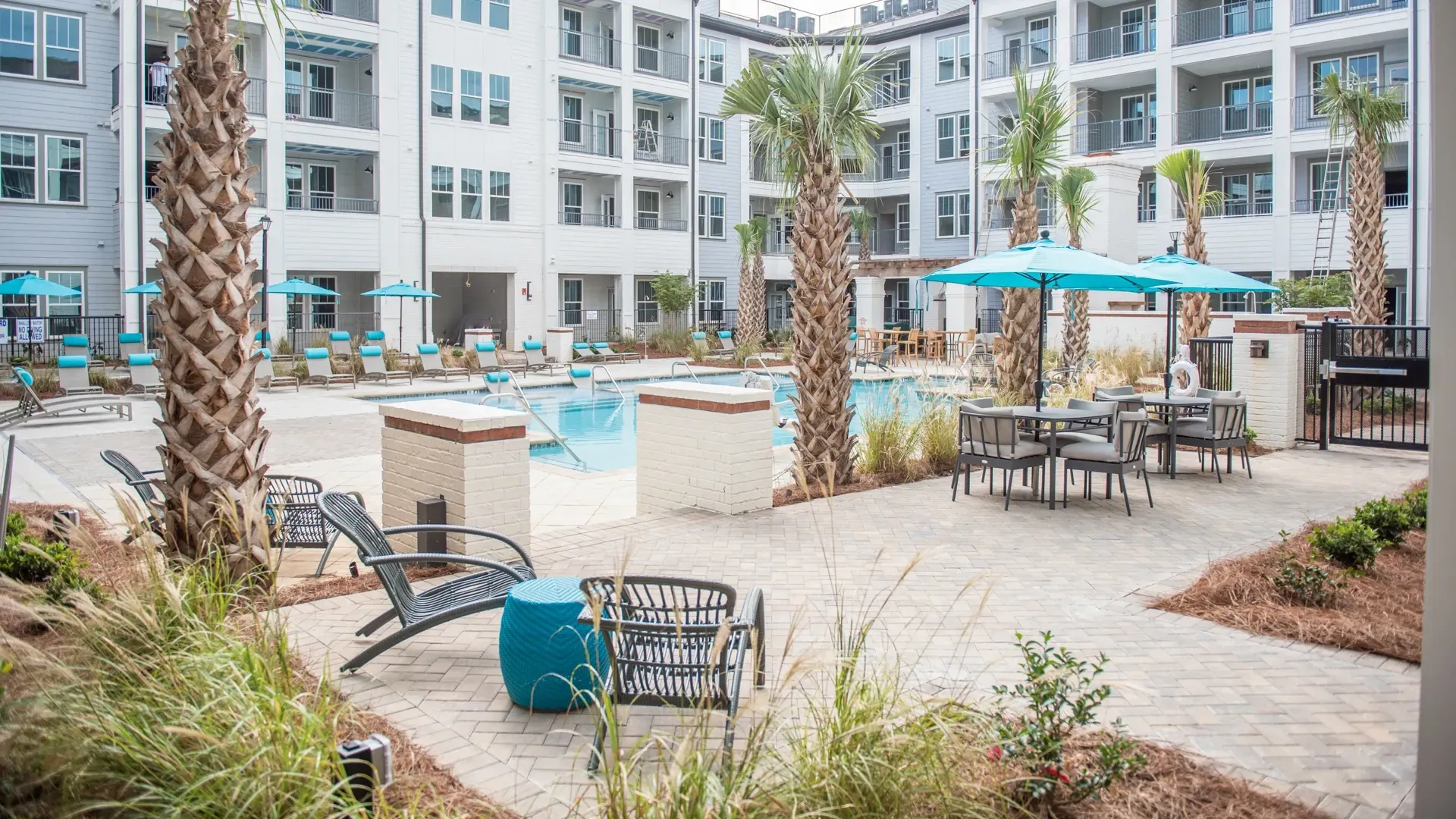 Resort-style swimming pool and lounge area with palm trees and seating.