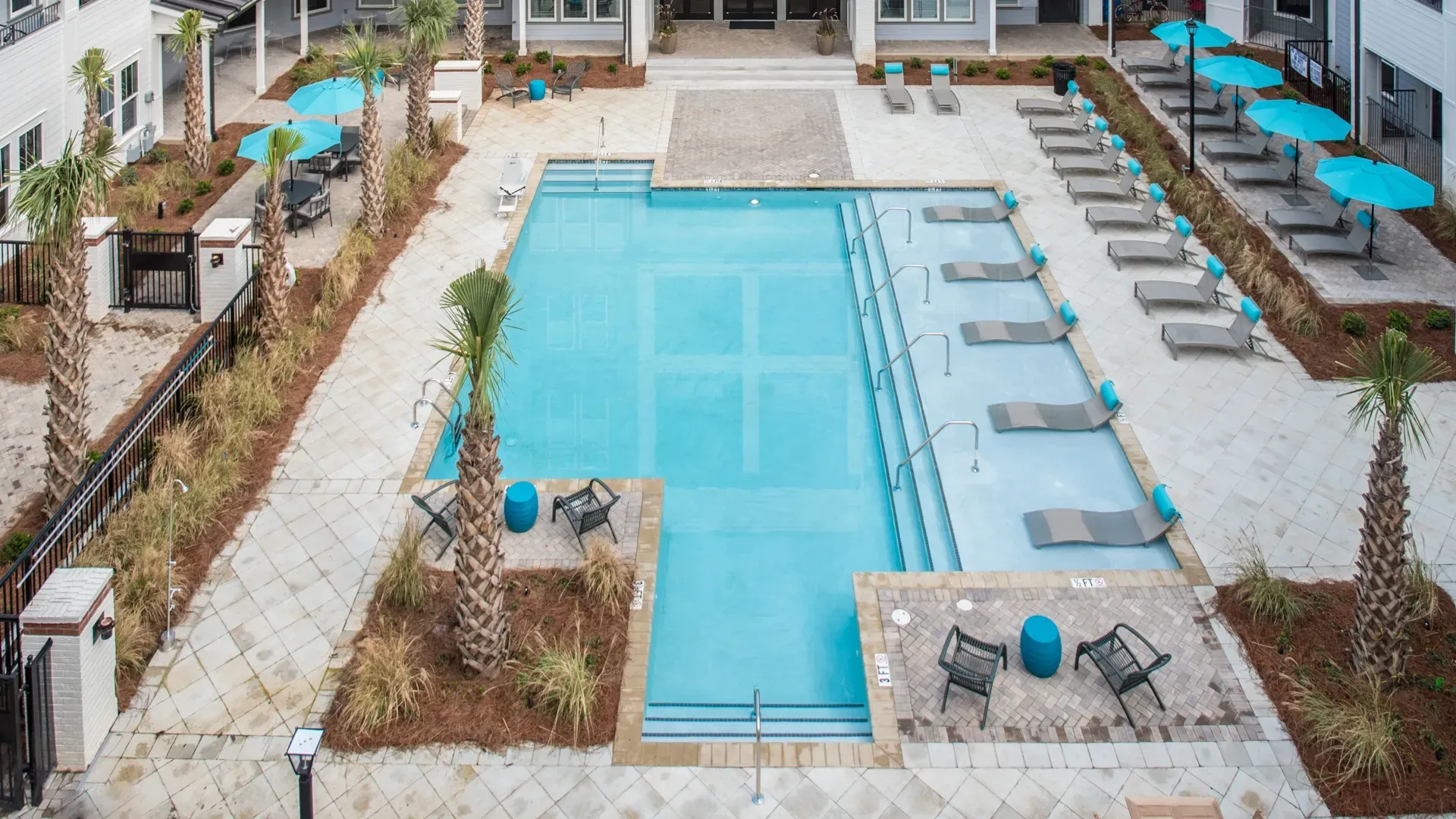 Luxury apartment complex pool area with lounge chairs and umbrellas.