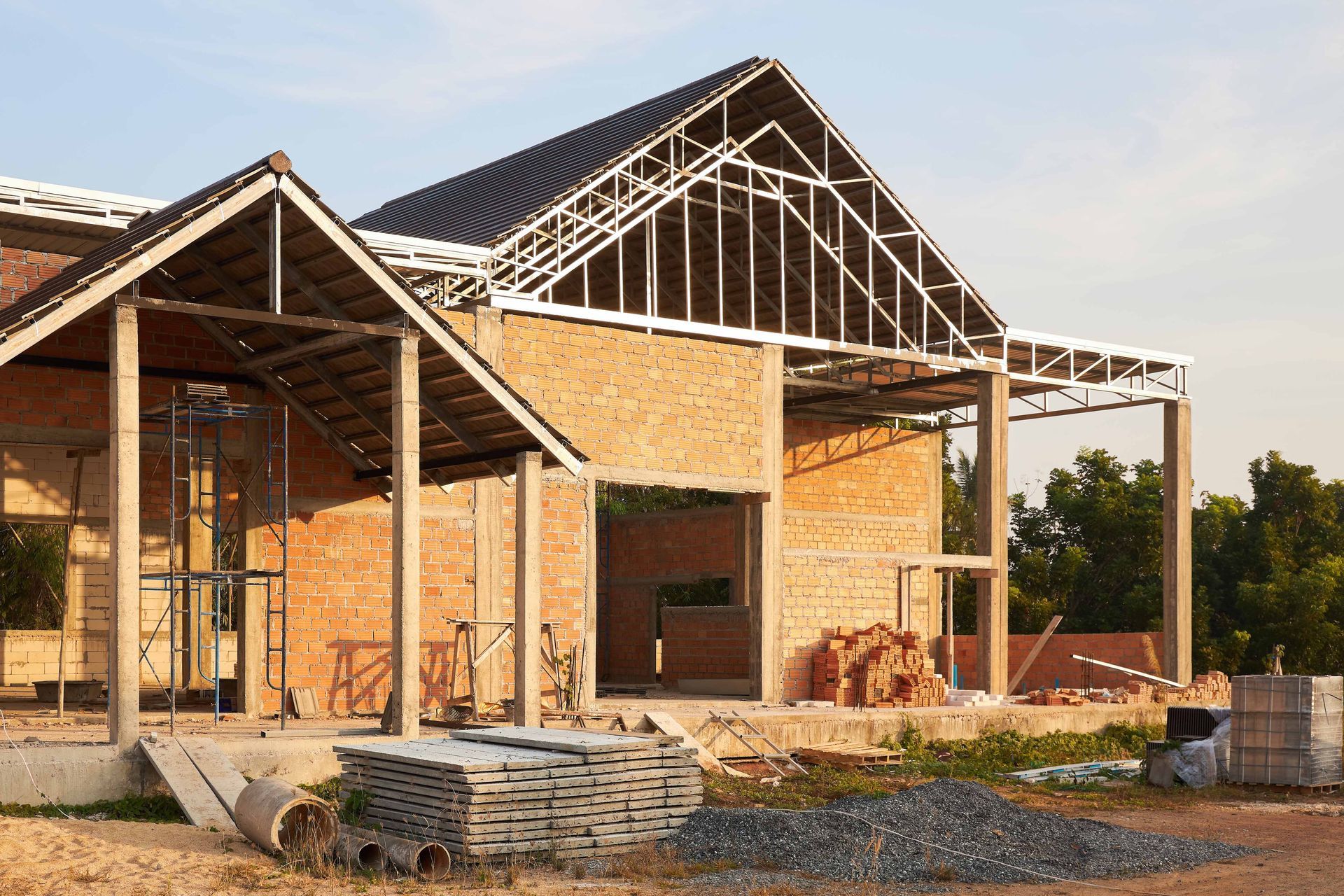 Building under construction, brick walls, steel frame roof, piles of bricks and building materials.