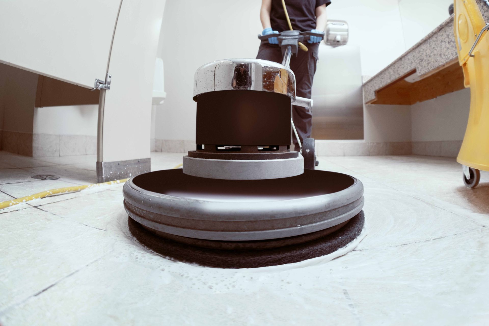Person using a floor buffer to clean a tiled floor in a room.