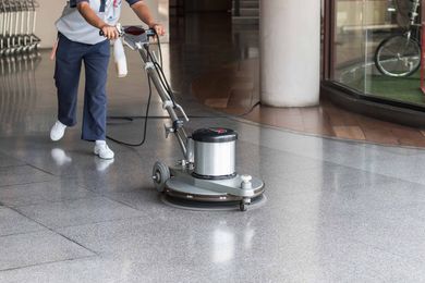 Person using a floor buffer to clean a speckled floor in a commercial building.