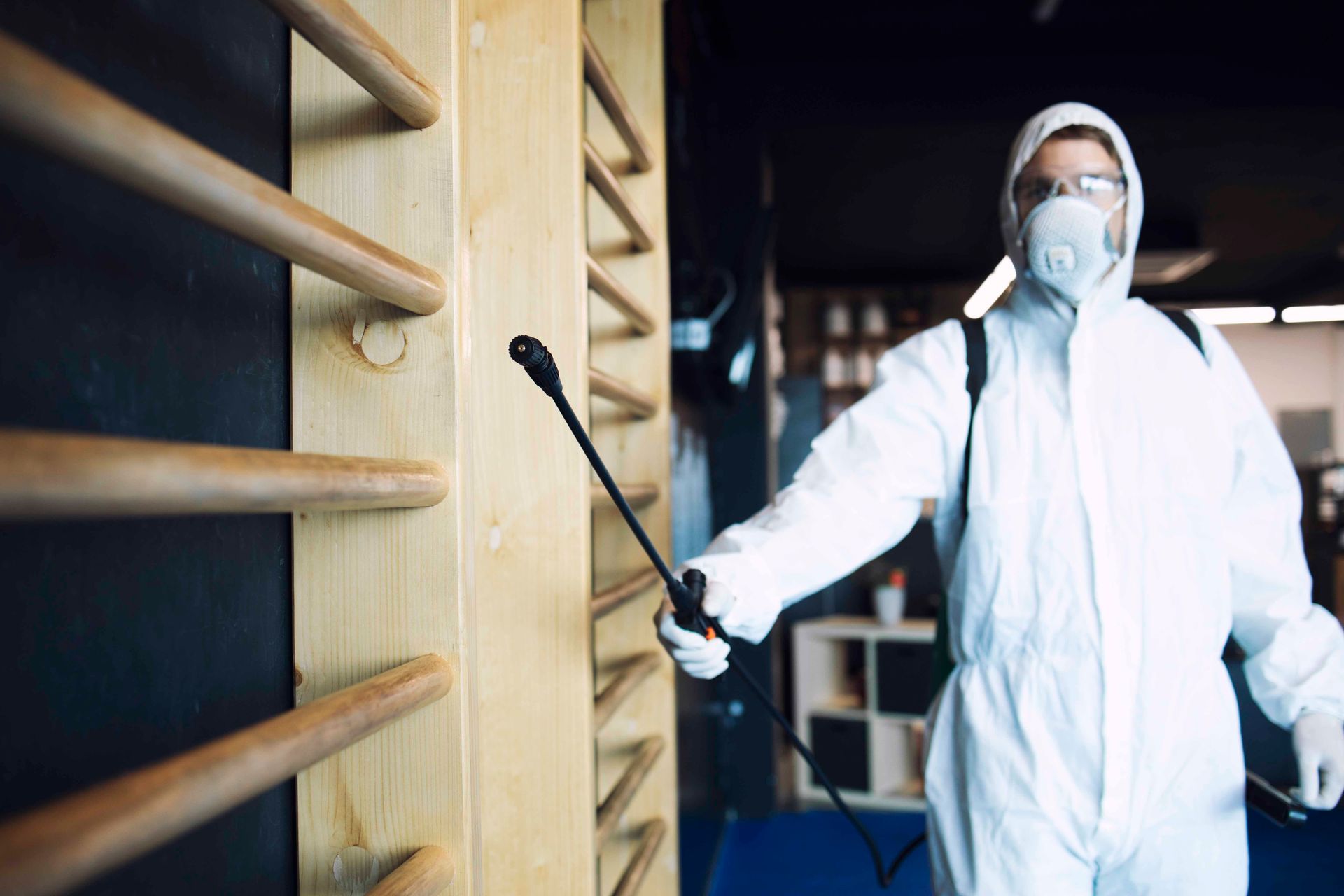 Person in hazmat suit disinfecting a wooden wall with a sprayer.