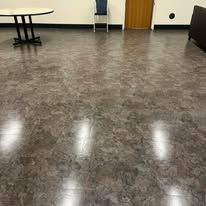 A shiny, mottled brown floor in a room with a table, chair, and a door.