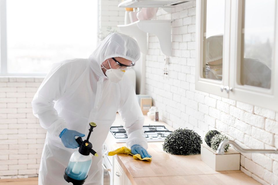 Hand using a soapy sponge to clean a white surface, removing dark grime and leaving a foamy residue.