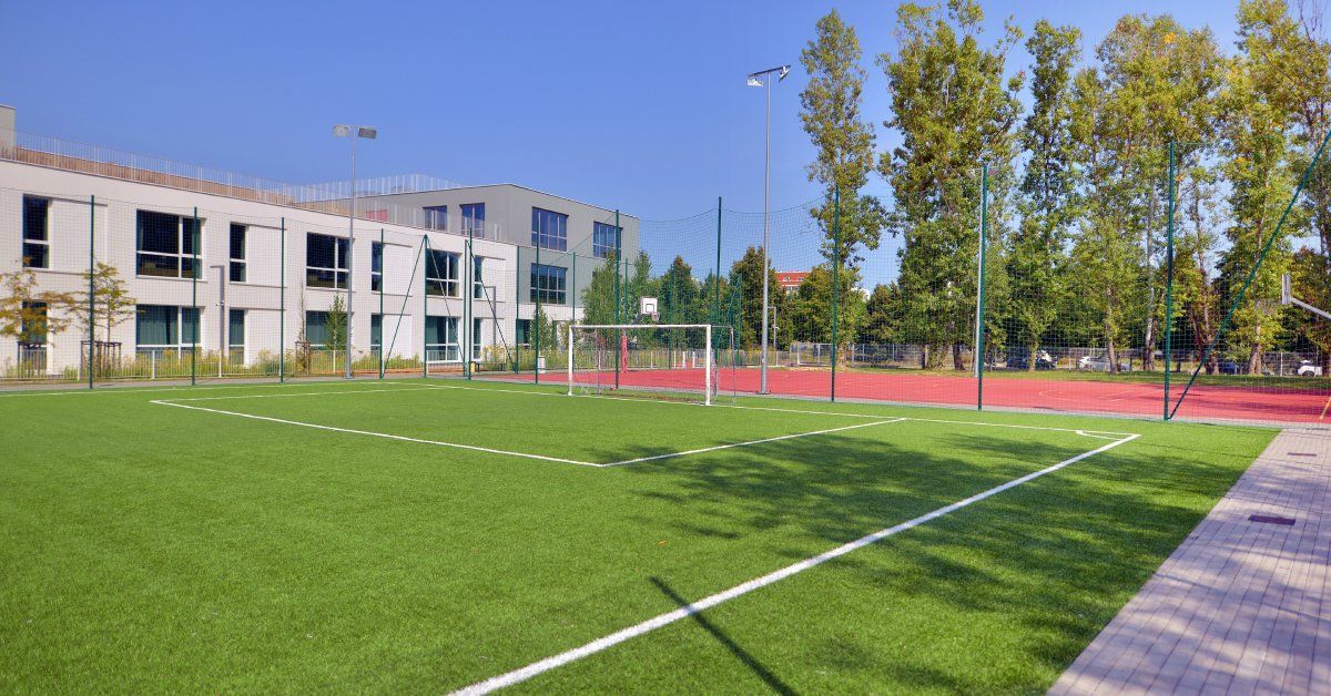 An artificial turf soccer field behind the school with a white goal net and white field lines. It's a sunny day outside.