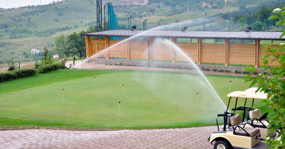 A commercial property with a patch of turf grass. There are two in-ground sprinklers on and watering the turf.