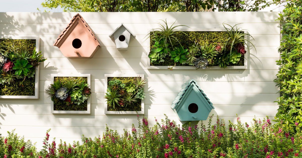 A backyard vertical garden with hanging elements on the white wooden fence. There are geometric shaped potting units.