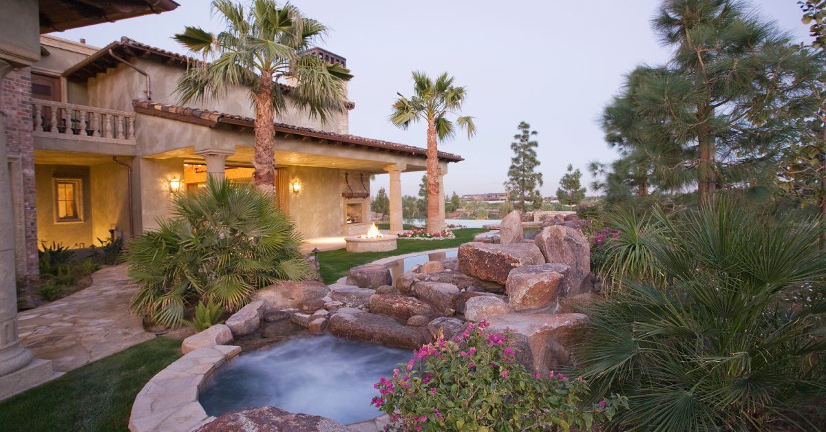 A beautiful Californian backyard with a water feature pouring into a stone jacuzzi feature. There are also palm trees.