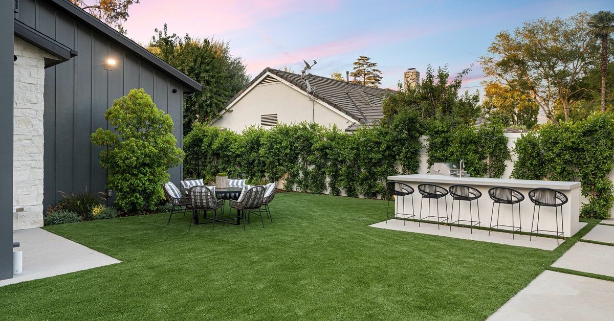 A beautiful backyard with synthetic turf, patio furniture, and a black house on the left. The sunset