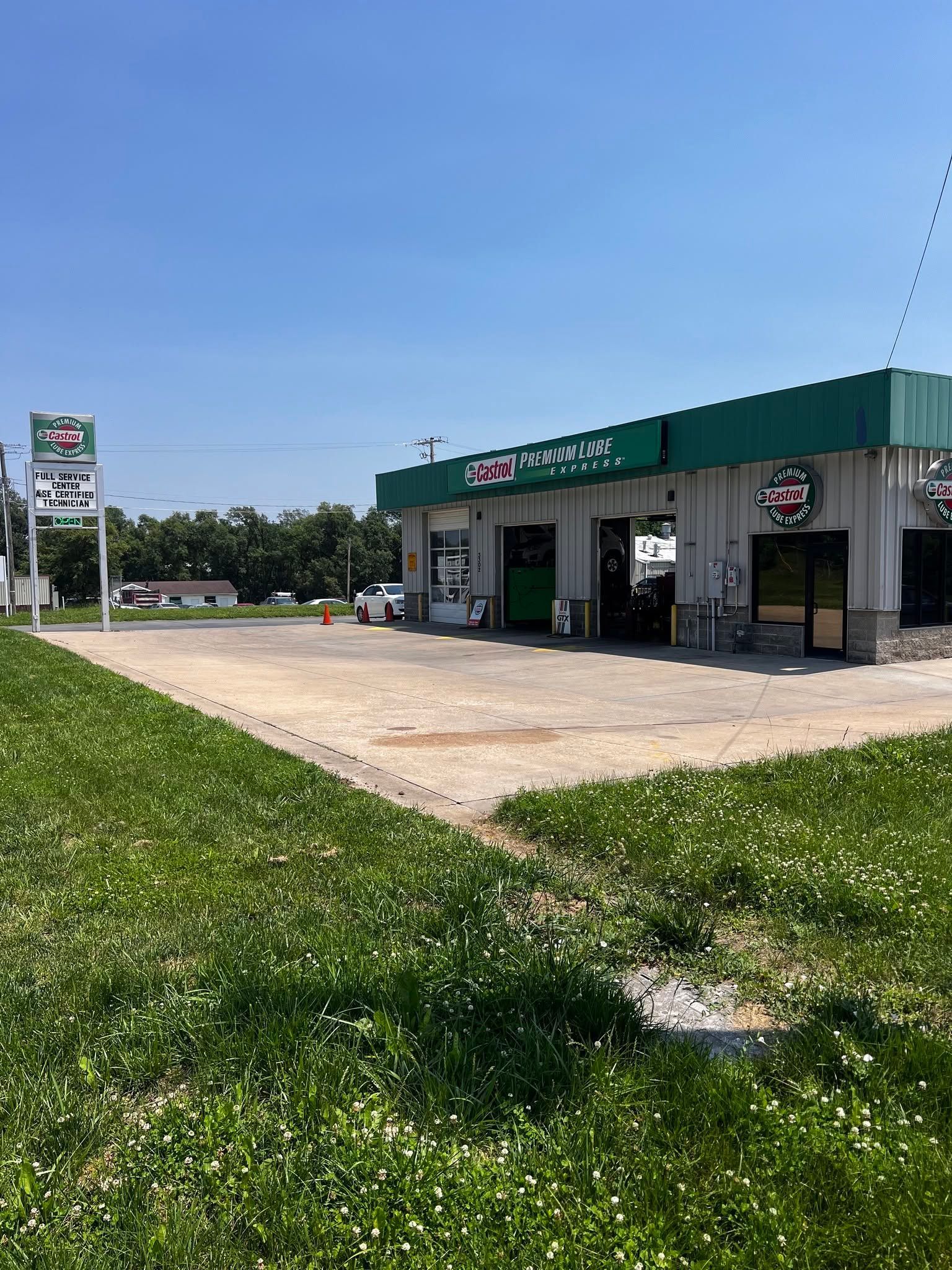 Small roadside convenience store with green awning and gas pumps beside a grassy lot under a clear blue sky | Castrol Pro-Lube of St. Joe