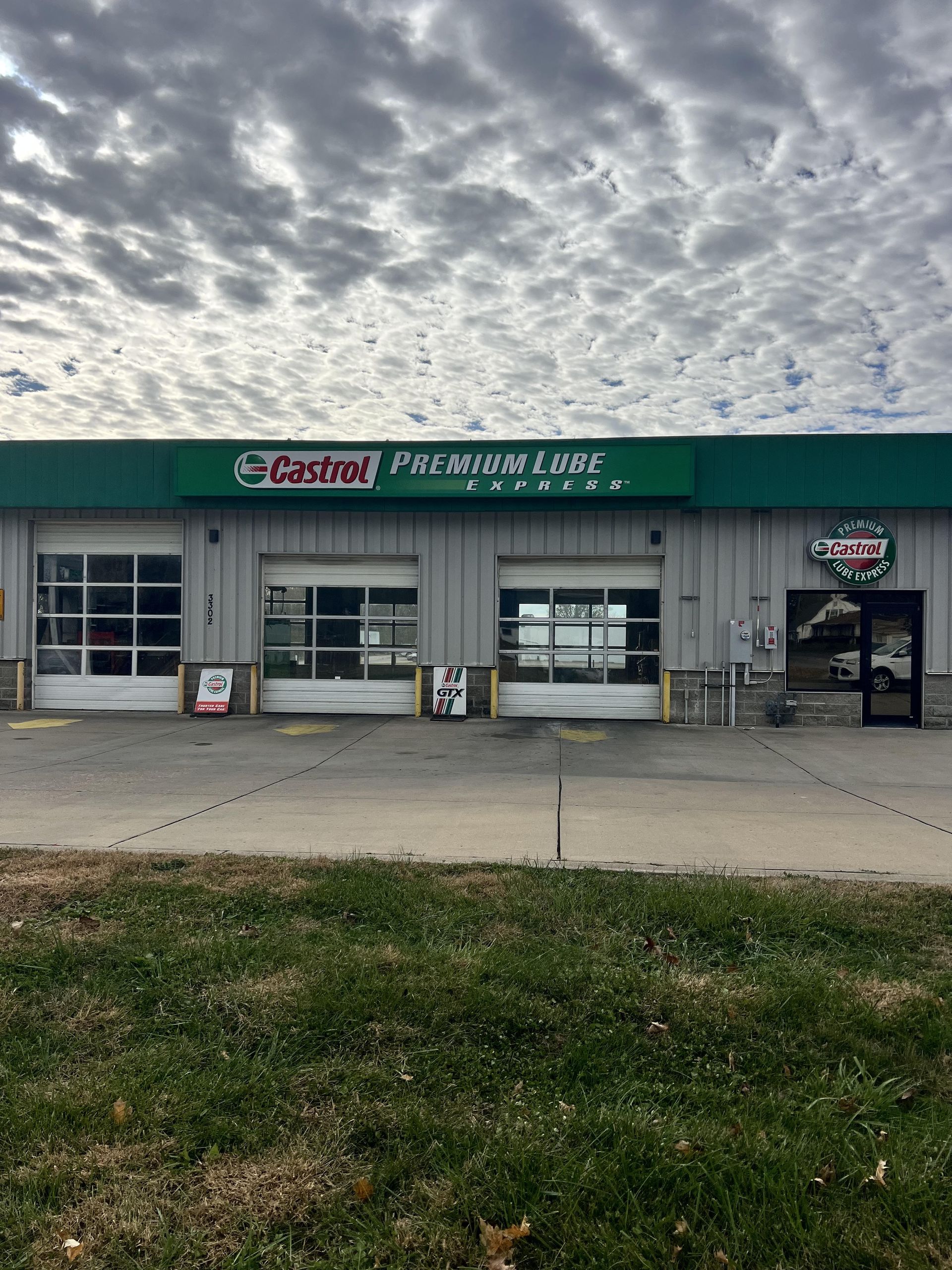 Auto repair shop storefront under a cloudy sky, with three garage bays and a Castrol sign | Castrol Pro-Lube of St. Joe