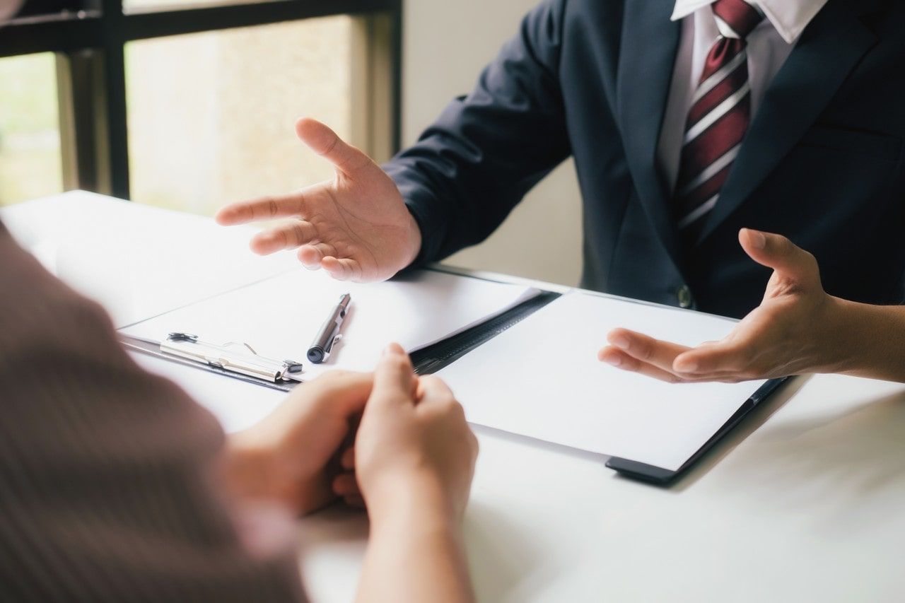 A man in a suit and tie is sitting at a table talking to a woman.