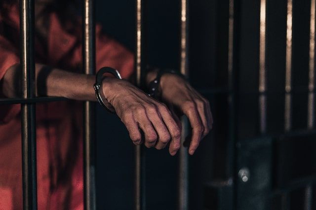hands in cuffs of person behind bars