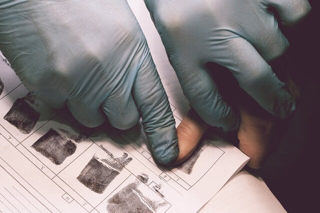 A person wearing blue gloves is looking at fingerprints on a piece of paper
