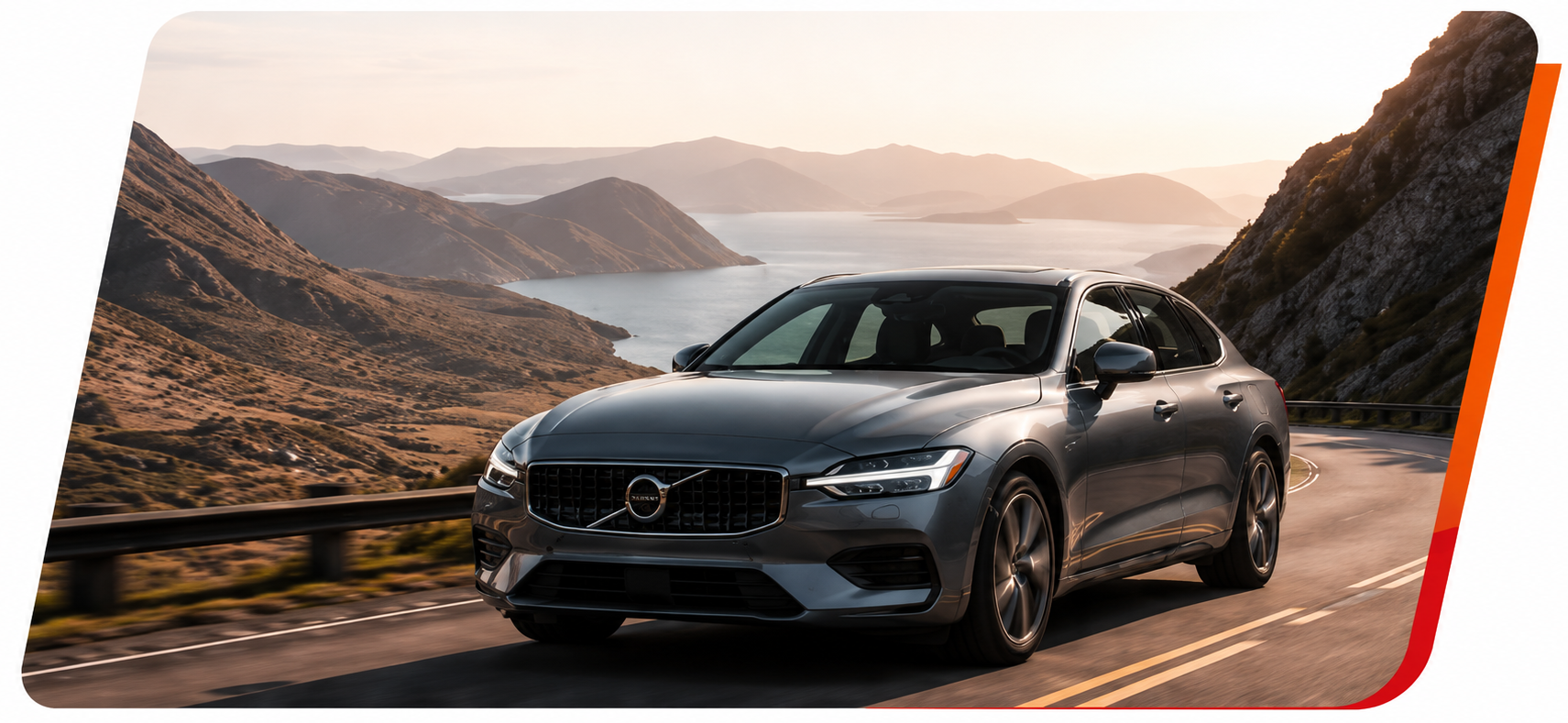 Silver Volvo sedan driving on a mountain road beside a lake at sunset