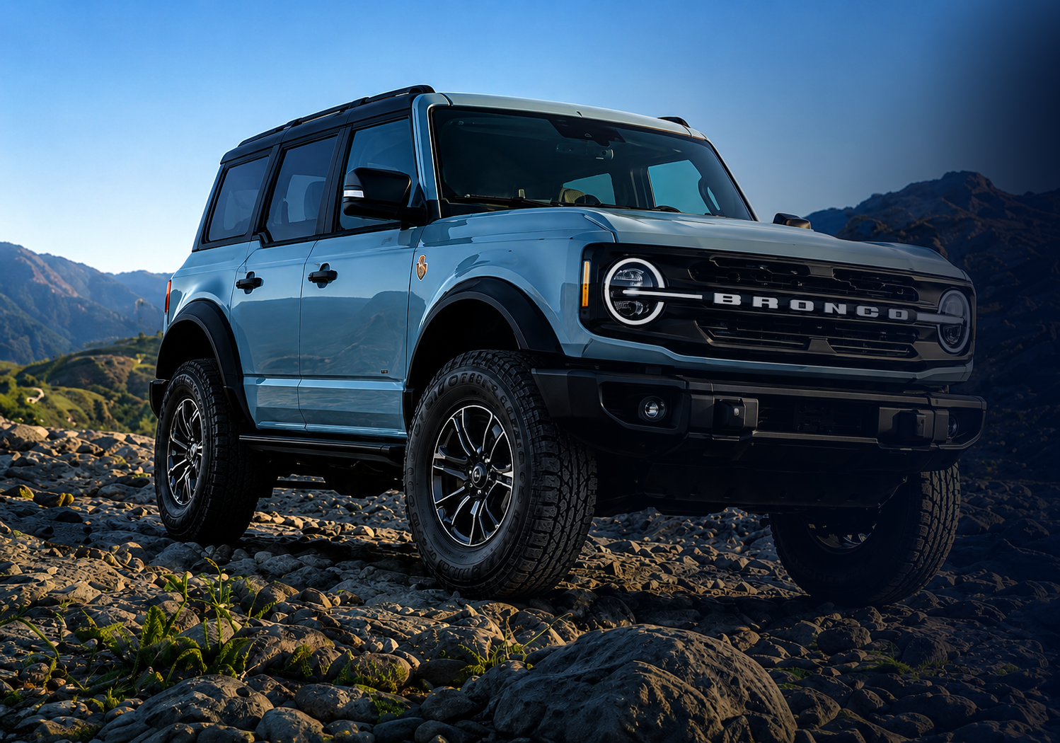 Silver Ford Bronco on rocky terrain with mountains in the background at dusk