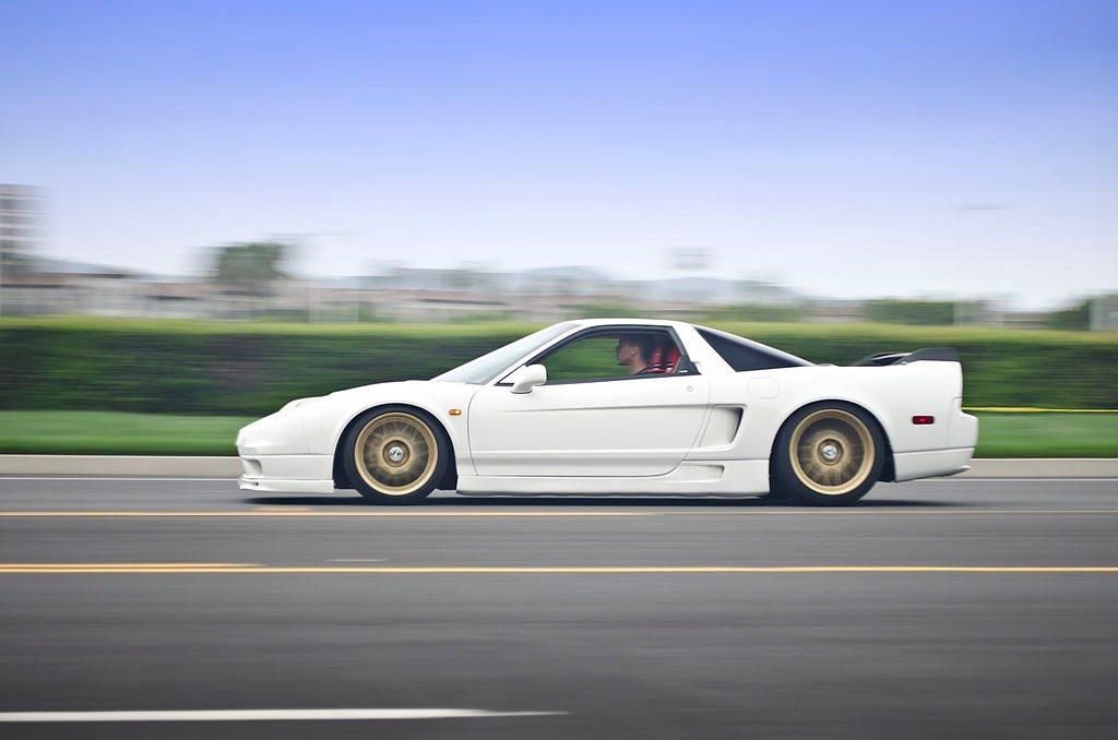 White sports coupe driving fast on a road with a blurred green background
