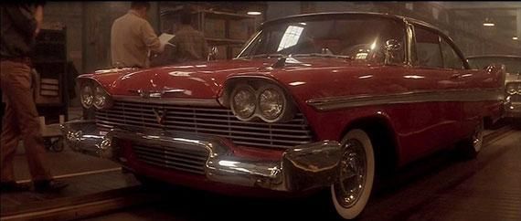 Red classic car parked indoors in a dim garage, with chrome details and a person nearby.