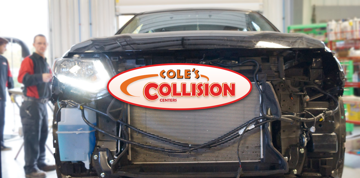 Damaged black car with a “Bob’s Collision” sign in a repair shop, front view.