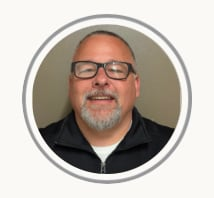 Smiling man with glasses and goatee in a circular profile photo on a beige background