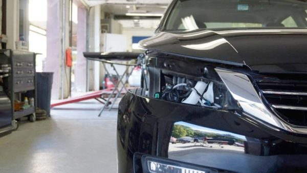 Black car in a repair shop, front bumper removed and headlights exposed