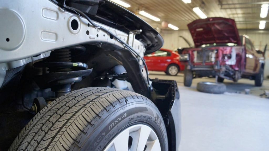 Close-up of a white car in an auto repair shop, with a maroon SUV in the background.