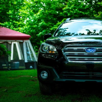 Black SUV parked on grass beside a red canopy tent in a green wooded area