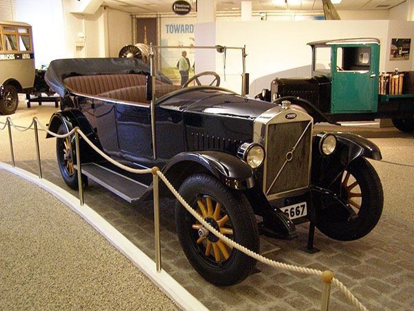 Vintage black car displayed in a museum, with a green vehicle in the background.
