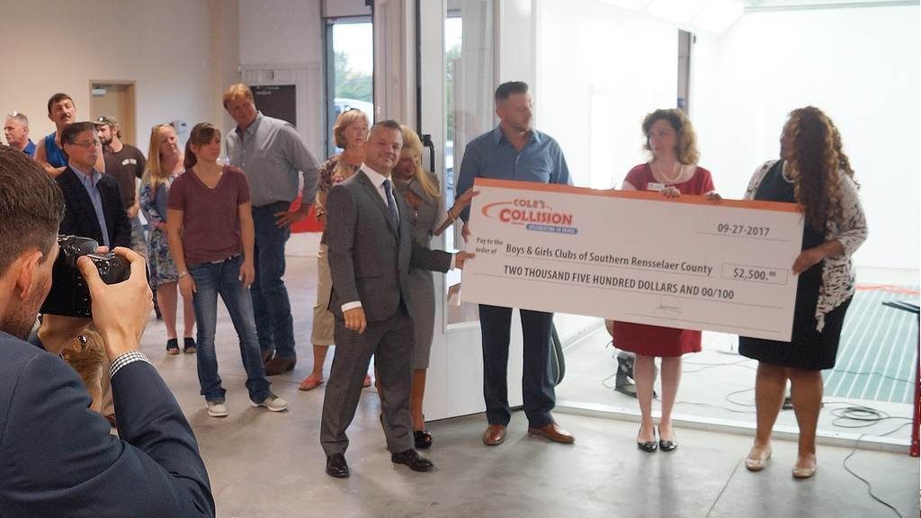 Group holding a large check at an indoor event, with people gathered around and a photographer in the foreground