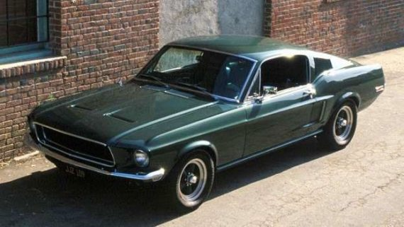 Dark green classic Ford Mustang parked beside a brick wall in a driveway.
