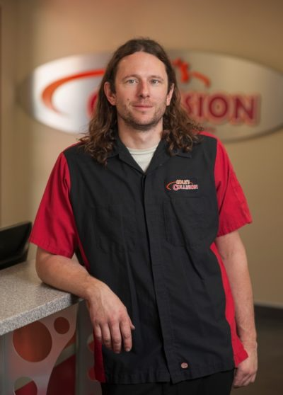 Man leaning on a counter in a black and red work vest inside a reception area