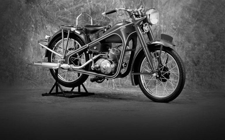 Black and white vintage motorcycle on a stand against a textured studio backdrop