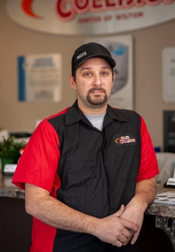 Man in a black cap and red-black uniform standing indoors at a service counter