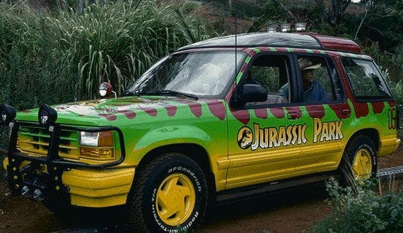 Jurassic Park Jeep in green and yellow, parked on a muddy road in tall grass