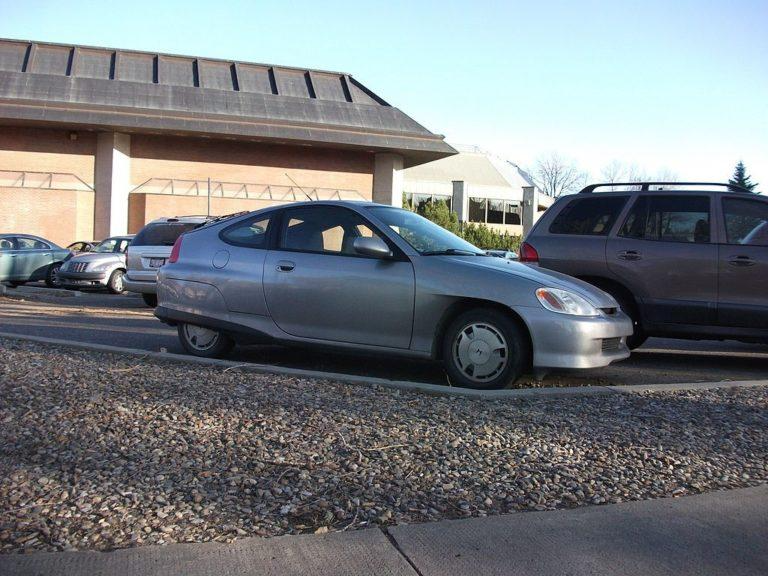 Silver car parked on gravel beside a brown SUV in front of a brick building