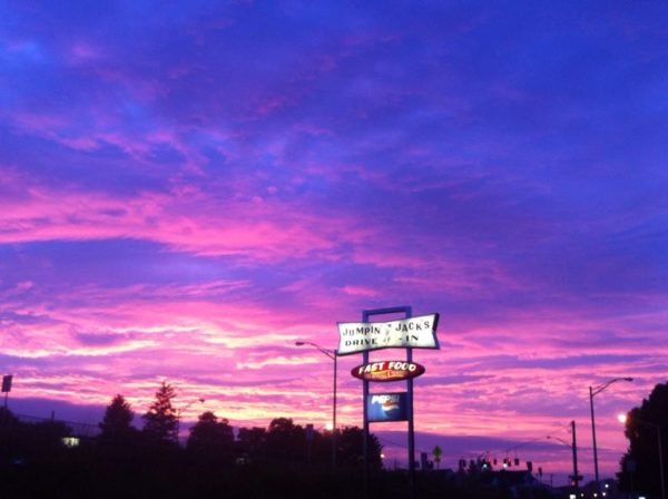 Pink and purple sunset over silhouetted trees with a roadside sign