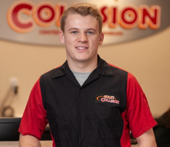 Smiling employee in red-and-black work shirt standing in a collision repair shop lobby