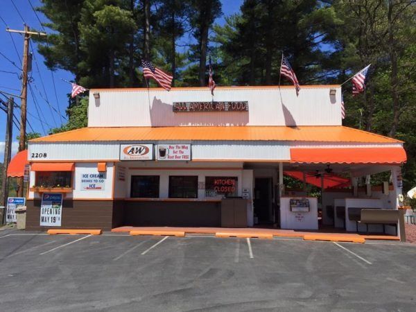 Small roadside restaurant with orange awnings and American flags, viewed from a parking lot