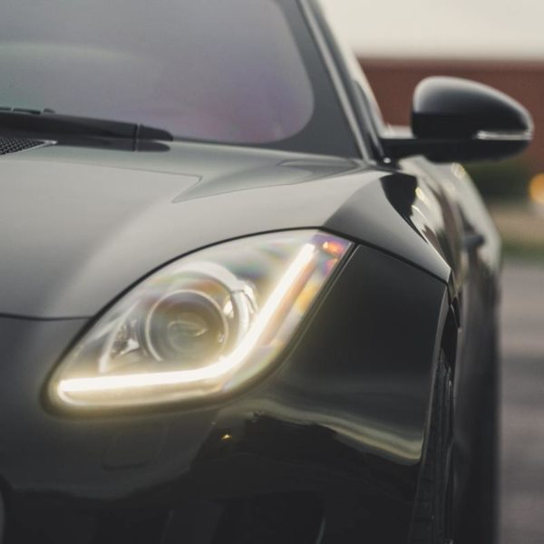 Close-up of a black sports car’s front headlight and side mirror on a road