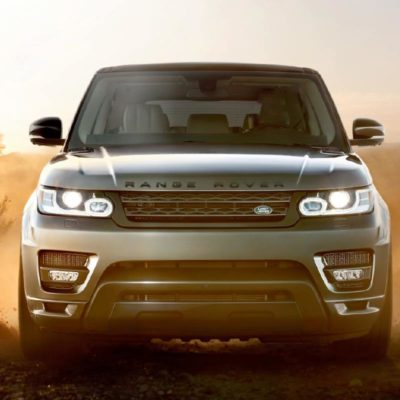 Front view of a silver Range Rover SUV driving through dust in a rugged outdoor setting