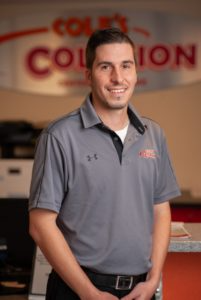 Man in a gray polo shirt standing indoors in front of a blurred company sign.