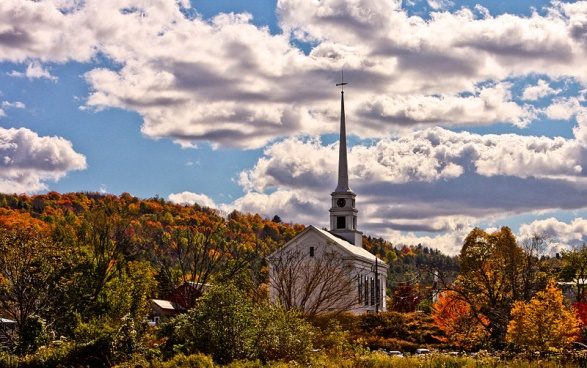 White church steeple above autumn trees under a cloudy blue sky