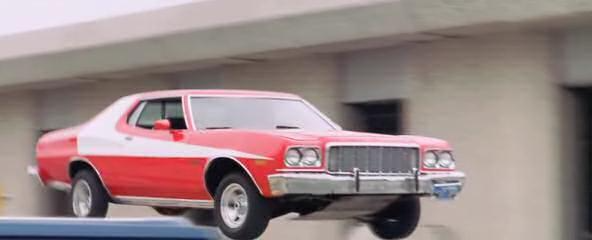 Red classic car jumping over a gap on a city street, side view.