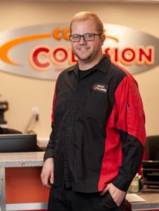Man in black and red work shirt standing at a reception desk with a blurred office sign behind him