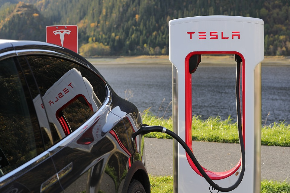 Black Tesla charging at a white Tesla Supercharger by a lake