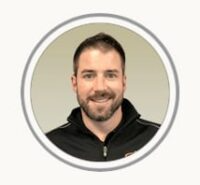 Portrait of a smiling man in a black zip-up jacket against a neutral background