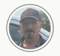 Man wearing a dark cap and jacket, standing beside a vehicle in a circular profile photo